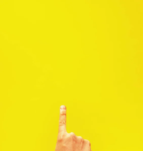 A closeup of a person pointing up isolated on a yellow background with space for te