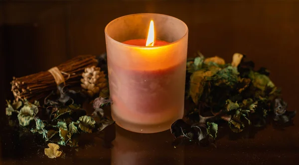 A closeup shot of a lighted candle with dried petals on a crystal glass