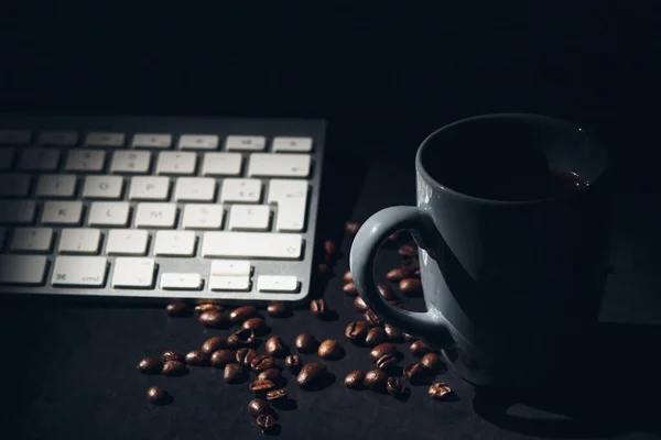 キーボードと豆で囲まれたホットコーヒーのカップの選択的なフォーカスショット ホームコンセプトからの仕事 — ストック写真