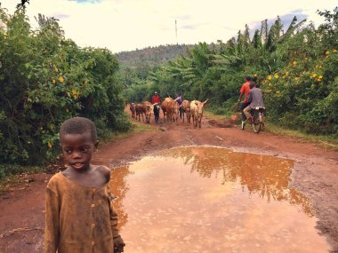 KIRUNDO, BURUNDI - Jun 03, 2017: A kid standing in front of a large puddle on a dirt road in Northern Burundi clipart