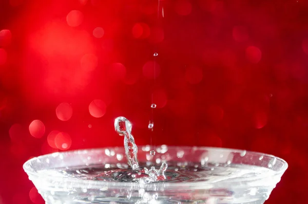 Gotas Água Caindo Copo Cheio Água Fundo Bokeh Vermelho — Fotografia de Stock