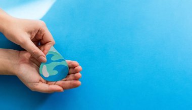 A view of woman hands holding paper cut water drop on a blue background - World Water Day clipart