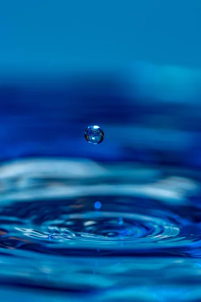 水の上に跳ねる水滴の驚くべき垂直ショット 青の背景 — ストック写真