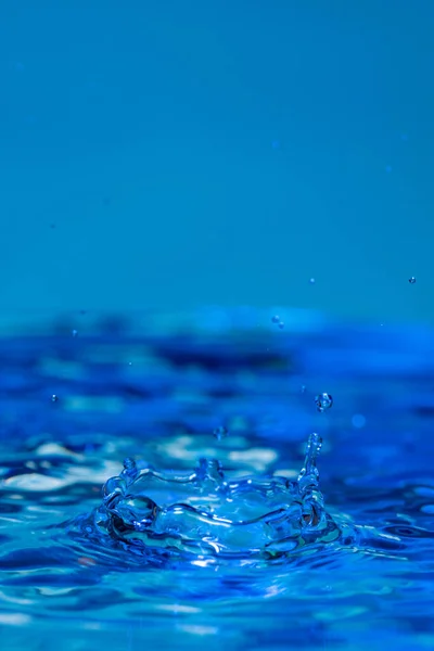 水滴在水面上跳跃的令人惊奇的垂直镜头和飞溅的蓝色背景 — 图库照片