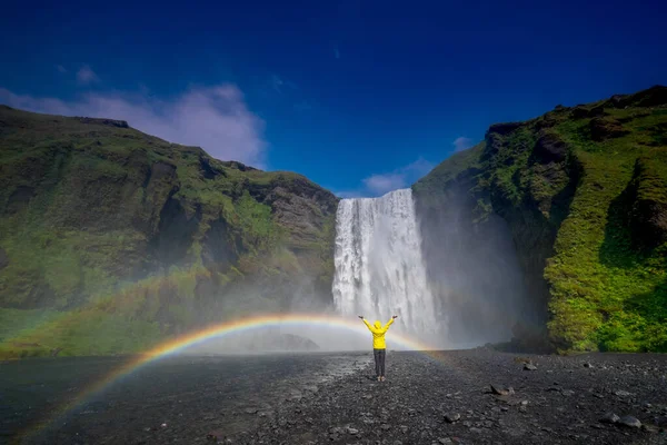 A joyful person enjoying the beautiful view of the rainbow at the Skogafoss waterfall in Iceland