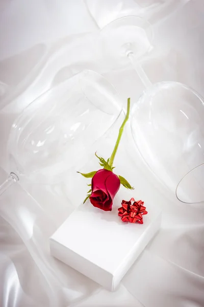 一朵红玫瑰 一个礼品盒 白色纺织品上的酒杯 — 图库照片