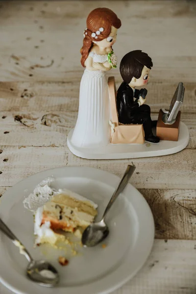一张与新郎和新娘在木桌上一块蛋糕旁的可爱雕像的垂直照片 — 图库照片