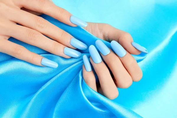 A closeup shot of a female\'s hands with blue nail polish on a blue silk fabric