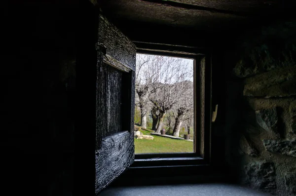 An interior view from the window of a rustic house towards a beautiful garden with trees