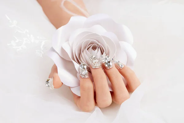 A closeup shot of a female\'s hands with diamonds on the nails holding a white rose