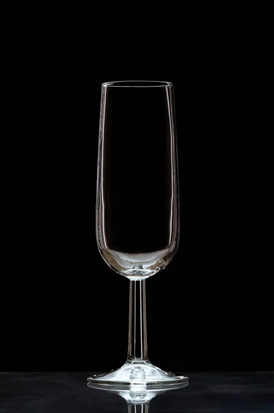 一个垂直的特写 一个空的香槟酒杯在一个黑色背景上隔绝的反光表面上 — 图库照片