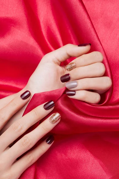 赤い絹織物にネイルポリッシュで女性の手の垂直ショット — ストック写真