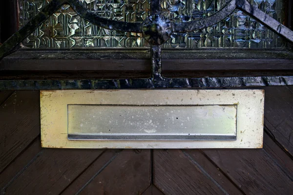 A closeup of a mail slot on a wooden door