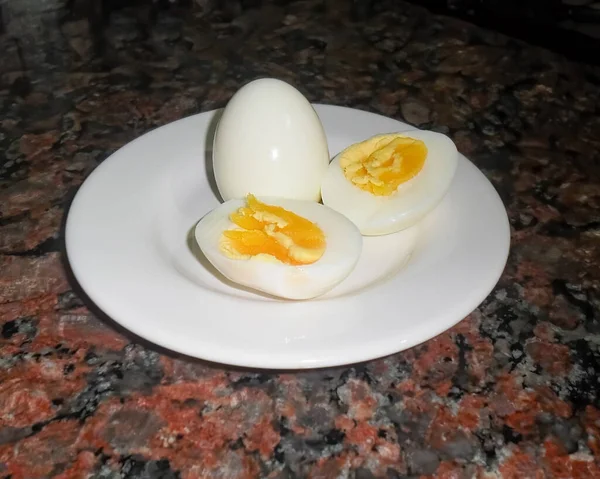 A high angle shot of two boiled eggs on a white plate, one in halves. showing yolk. Dark granite background.