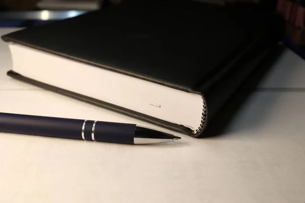 在白色表面的黑色笔记本旁边的一支钢笔的特写 — 图库照片