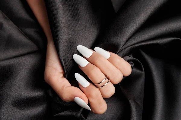 黑缎子一只有长长的白色指甲的雌性手 手握着黑色缎子织物 — 图库照片