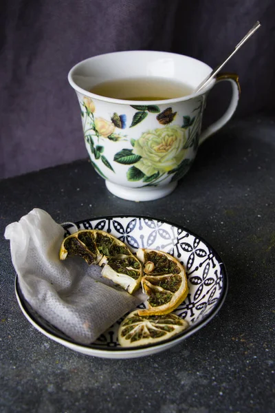 A vertical shot of a cup of fresh tea and a saucer with lemon and t