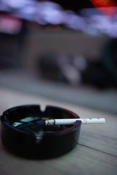 烟灰缸里一根香烟在木制桌子上的烟灰缸里的垂直拍 — 图库照片