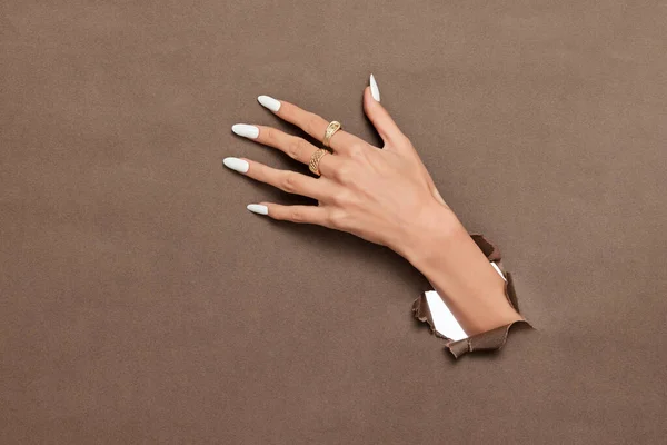 長い白い釘と茶色の紙の背景から突き出た黄金のリングを持つ女性の手 — ストック写真