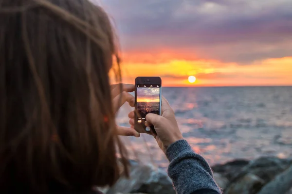 彼女の携帯電話で海で日没の写真を撮るから女性の選択的ホットスポット — ストック写真