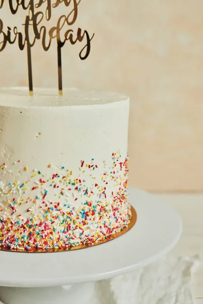 A vertical shot of a cake with a \'\'happy birthday\'\' cake topper and sprinkles on a tray on the table