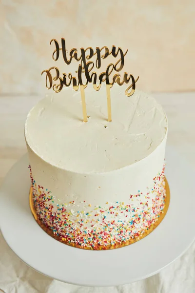 A vertical shot of a cake with a \'\'happy birthday\'\' cake topper and sprinkles on a tray