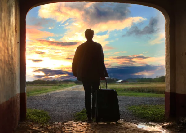 A male with a suitcase from the back looking at the beautiful sunrise with clouds