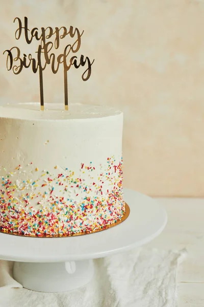 A vertical shot of a cake with a \'\'happy birthday\'\' cake topper and sprinkles on a tray on the table