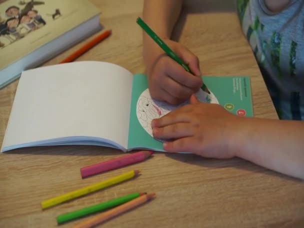 木製のテーブルでページを着色するためにカラフルな鉛筆を使用して若い男の子 — ストック動画