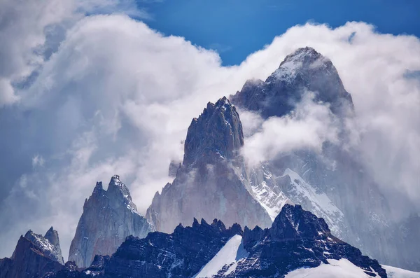 俯瞰着被蓬松的云彩环绕的陡峭的岩石和白雪覆盖的高山的景象是迷人的 — 图库照片