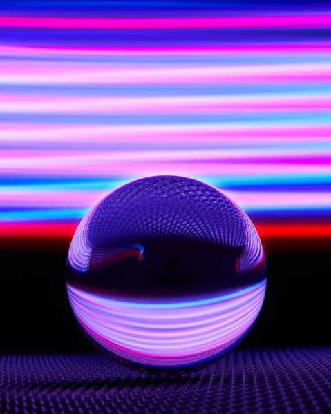A vertical shot of a reflective ball with an illuminated colorful background