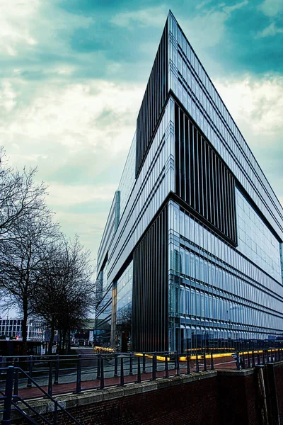 A vertical shot of a modern triangle building with glass in the cloudy sky background