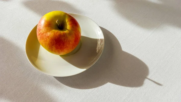 テーブルの上にその影が置かれたプレート上のリンゴの高角度ショット — ストック写真