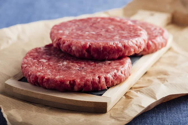 A closeup shot of fresh raw burger patties on a wooden board