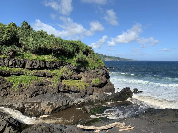 ハワイのマウイ島にある黒い火山岩と明るい緑の熱帯植物に波が飛び交う海の景色 — ストック写真