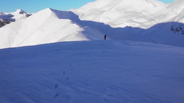 美しい冬の夕日に雪の山の上を歩く若い男 — ストック動画
