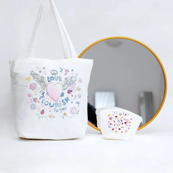 A closeup view of a white tote bag with a colorful print and a tiny bag int, and a mirror