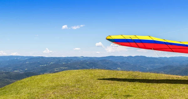 A wide-angle lens shot of a colorful hang glider\'s wing on a grassy landscape