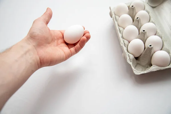 A male hand holding an egg with an egg carton on the tab