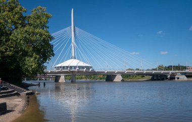 The Esplanade Riel bridge over a lake in a park under a blue sky and sunlight in Canada clipart
