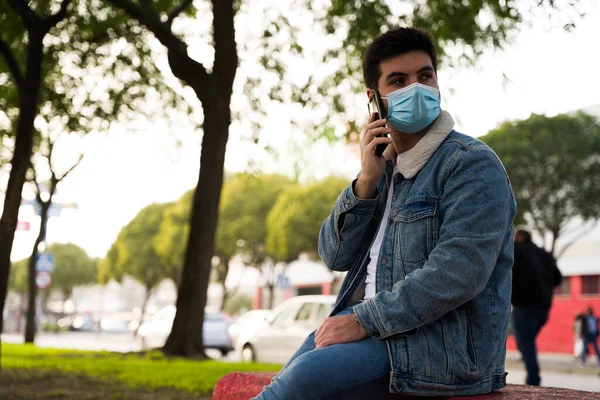 Tıbbi Maskeli Taş Bir Bankta Otururken Telefonla Konuşan Yakışıklı Bir — Stok fotoğraf