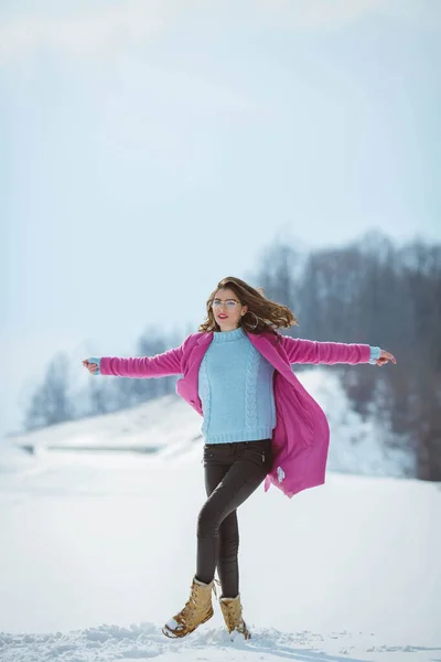 雪の中でポーズをとるピンクのコートでブルネットの女性の垂直ショット — ストック写真