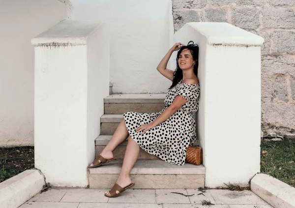 Smiling Caucasian Woman Polka Dotted Flowy Dress Sitting White Stairs — 스톡 사진