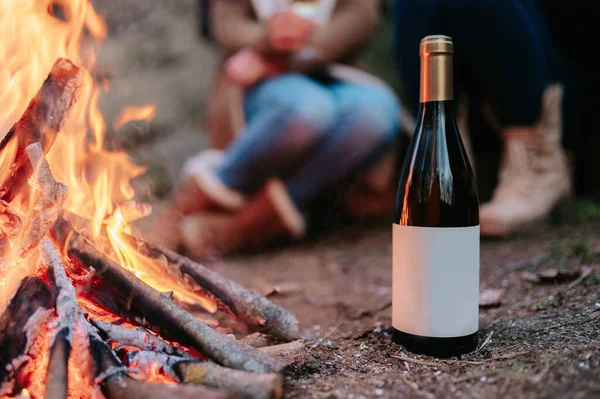 A close-up bottle of wine with copy space by the fire with people in the blurry background.