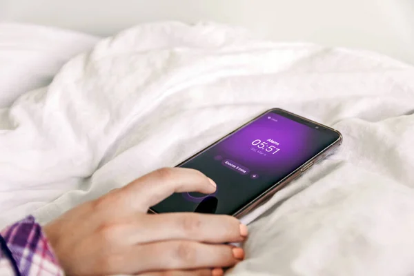 Close-up image of hand pressing dismiss button on alarm on mobile phone. Woman in bed, snooze, alarm clock, wake up, morning, early.