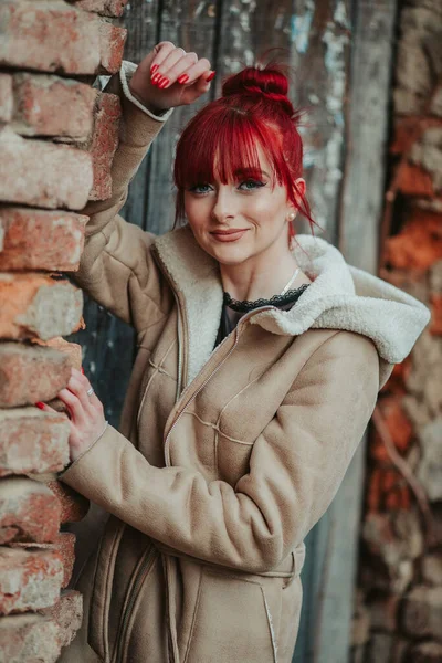 一幅美丽的红头发女孩的画像 她穿着一件温暖的棕色冬衣 手挽手靠在砖墙上 — 图库照片