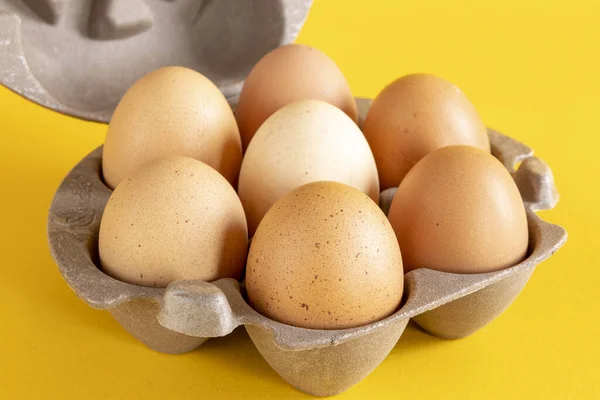 Closeup of half a dozen eggs in recycled paper carton box basket against a seamless yellow background