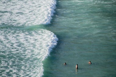 AUCKLAND, NEW ZEALAND - Feb 21, 2021: View of three tourists bathing near dangerous rip current at Piha beach, Auckland, New Zealand clipart
