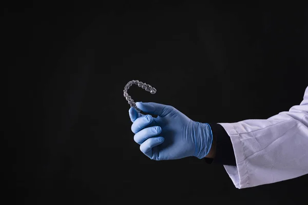 A closeup of hand in gloves holding a transparent mouthguard isolated on black background