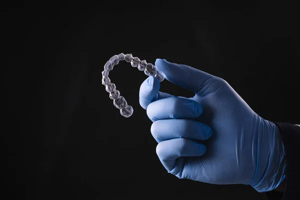 A closeup of hand in gloves holding a transparent mouthguard isolated on black background